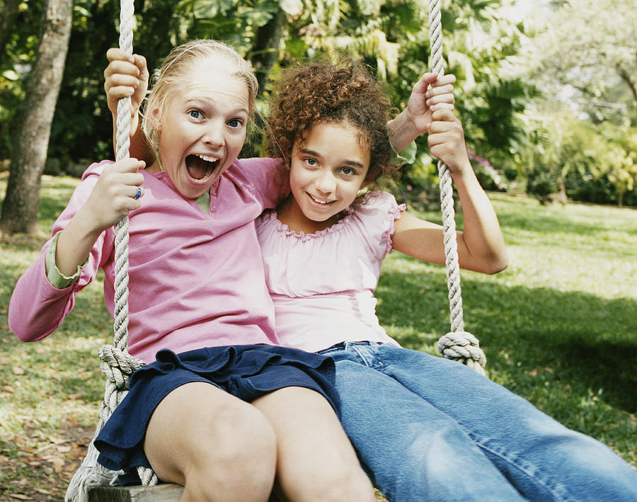 Two Young Girls Sitting Side by Side on a Swing Photograph by Digital Vision.