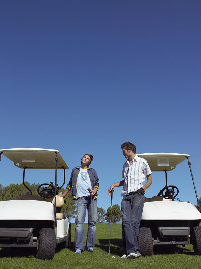 Two Young Men Standing by Golf Buggies and Holding Golf Clubs Photograph by Digital Vision.