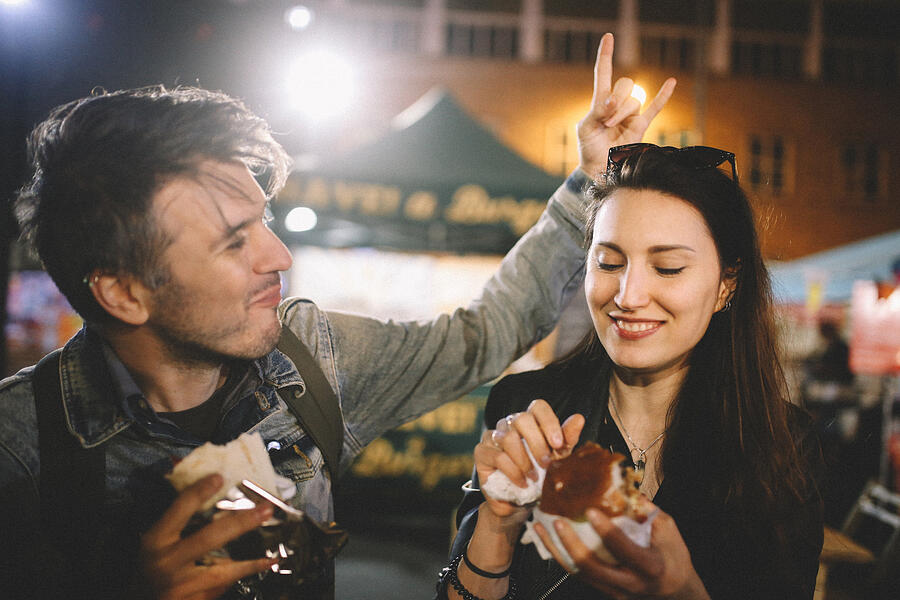 Two young people having fun eating street food in London at night Photograph by Lechatnoir