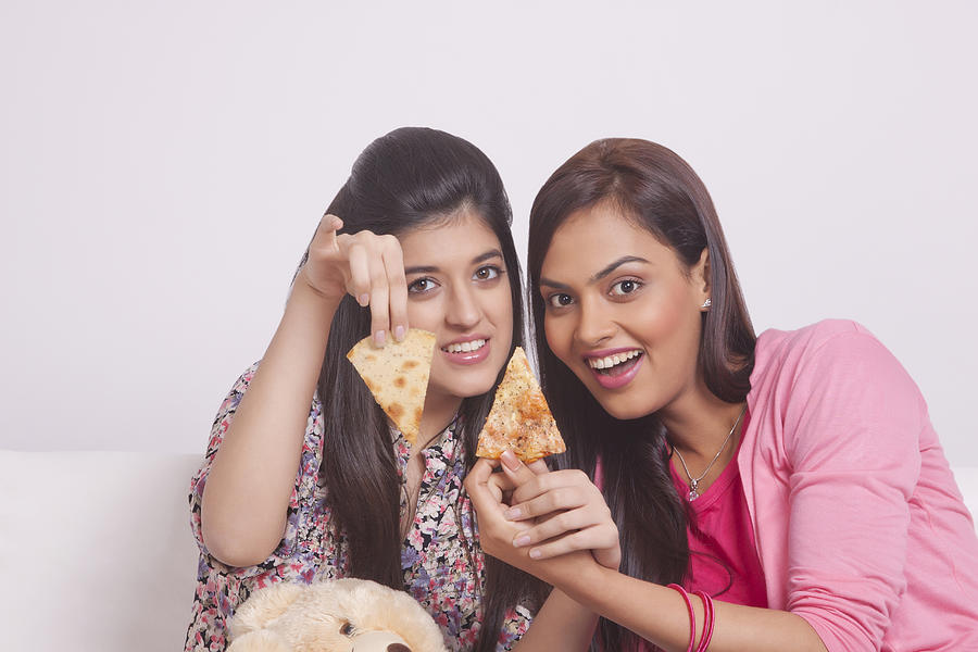 Two young women eating pizza Photograph by IndiaPix/IndiaPicture