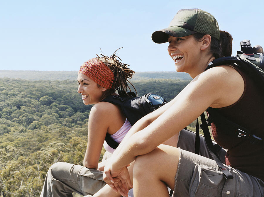 Two Young Women Relaxing From Hiking and Looking at the View Over Treetops Photograph by Digital Vision.