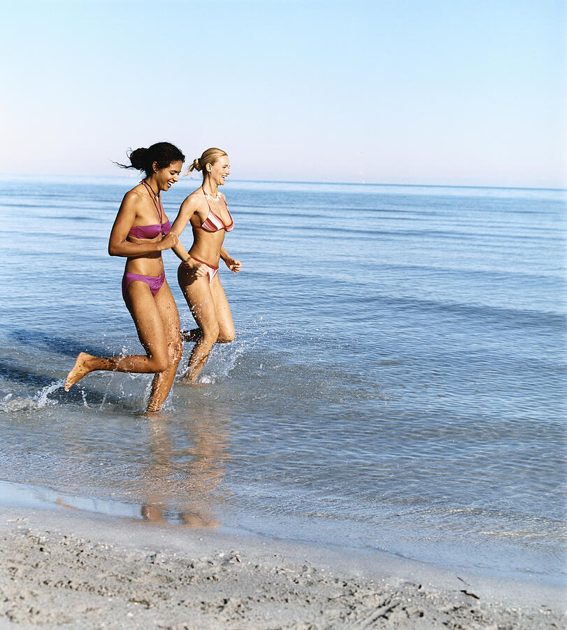 Two Young Women Running in the Sea Photograph by Digital Vision.