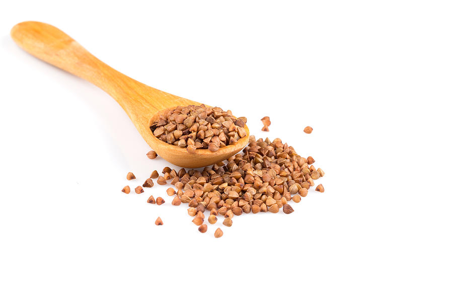 Uncooked buckwheat on wooden spoon. premium buckwheat groats on white background Photograph by R.Tsubin