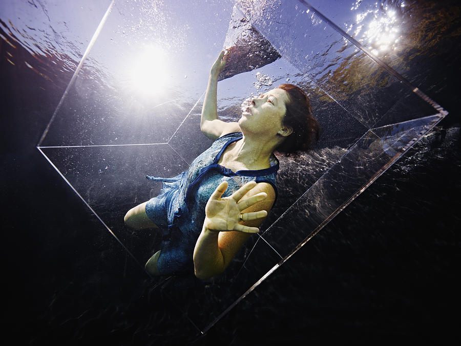Underwater view of woman in glass box looking up Photograph by Thomas Barwick