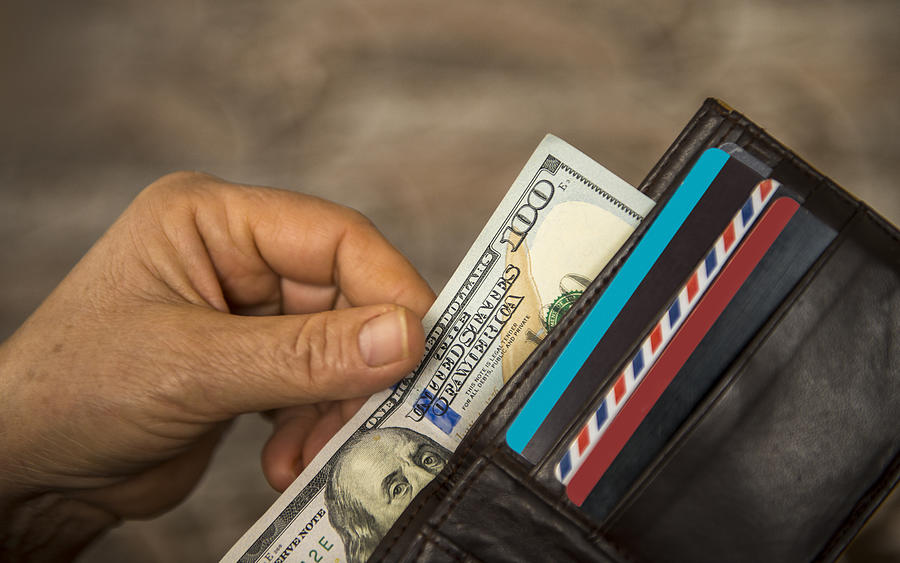 Unrecognizable mature man putting USA Dollar bill into wallet Photograph by CiydemImages