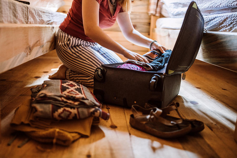 Unrecognizable woman packing luggage in log cabin Photograph by Pekic