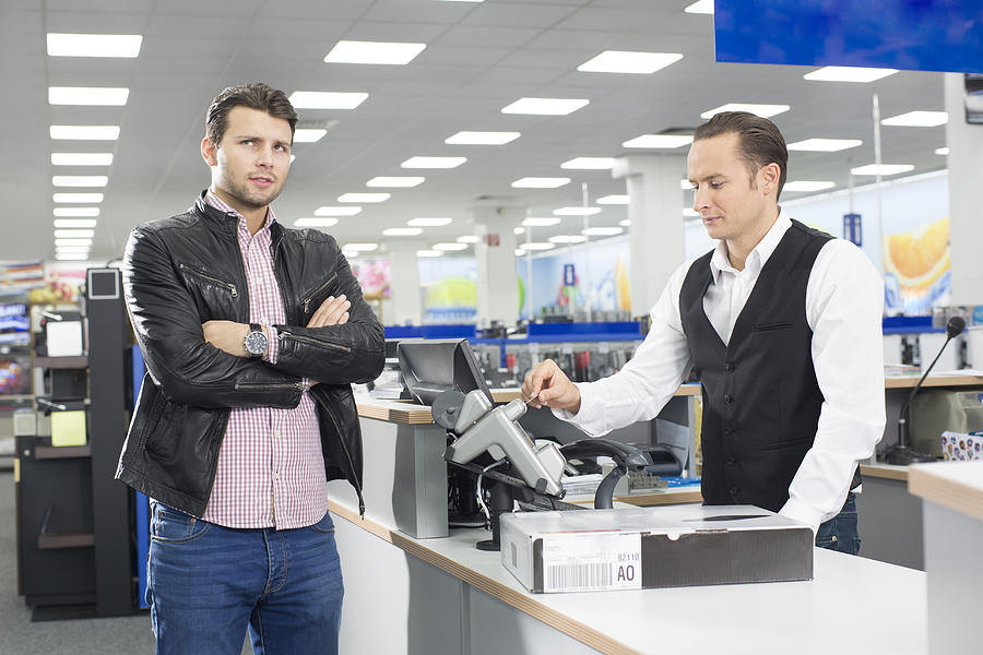 Unsure shopper paying with credit card in electronics store Photograph by Raygun