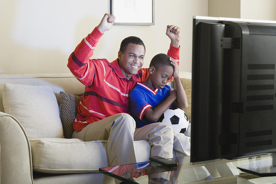 USA, California, Los Angeles, Father and Son (12-13) watching sports on tv Photograph by Rob Lewine