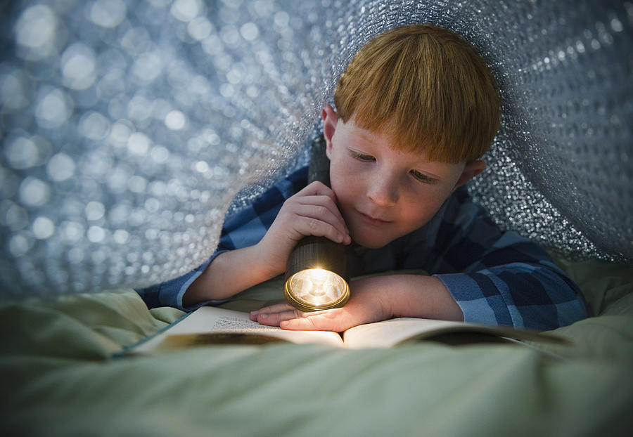 USA, New Jersey, Jersey City, Boy (8-9) reading book under bed covers Photograph by Tetra Images - Jamie Grill Photography