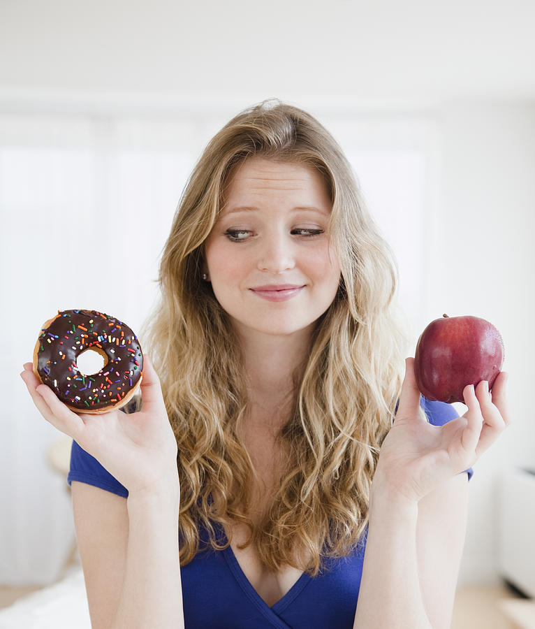 USA, New Jersey, Jersey City, Young woman choosing between donut and apple Photograph by Jamie Grill