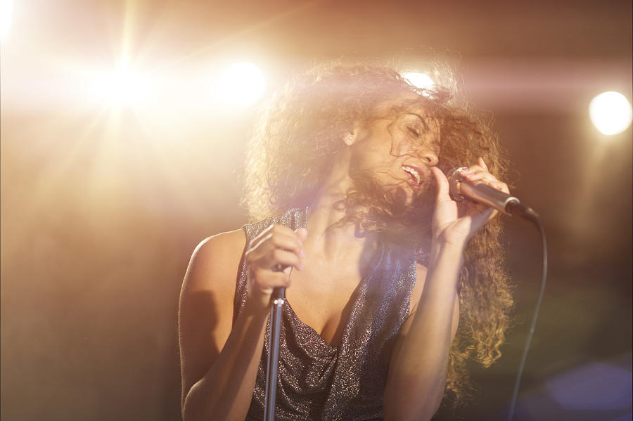 USA, New Jersey, Jersey City, Young woman singing in spotlight Photograph by Tetra Images