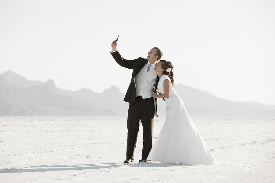 USA, Utah, Boneville Salt Flats, Bride and groom photographing themselves in desert Photograph by Fbp