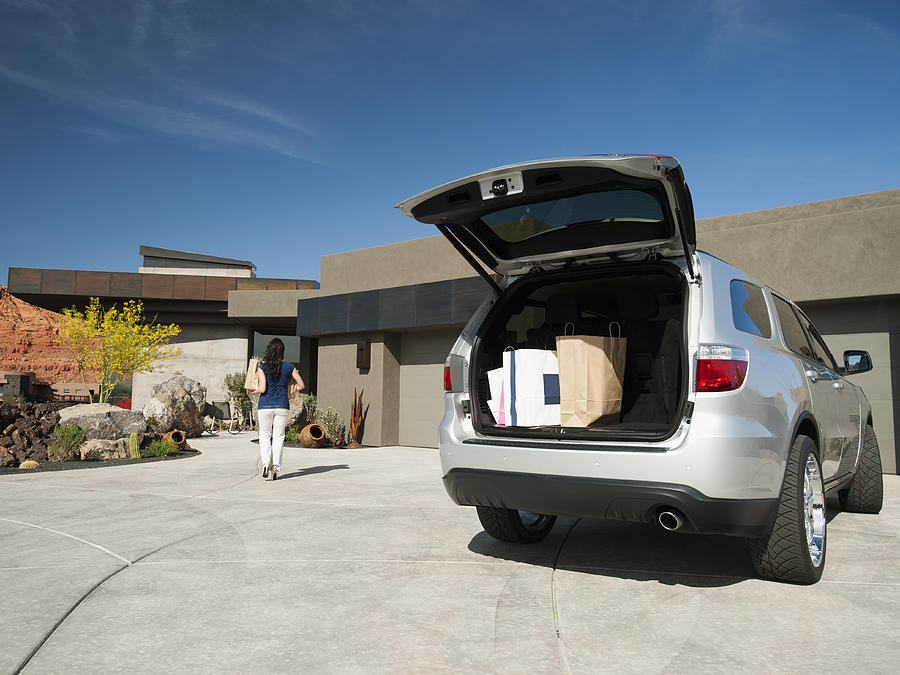 USA, Utah, St. George, Young woman unpacking shopping from car parked in yard Photograph by Erik Isakson