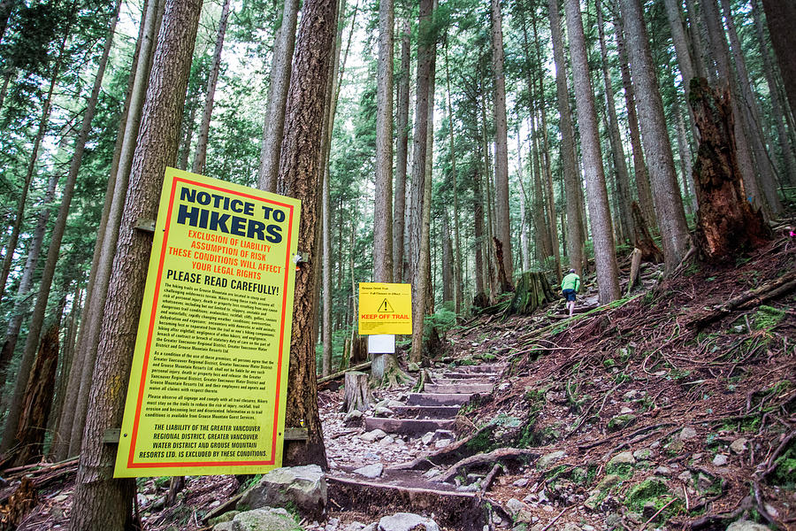 VANCOUVER, BRITISH COLUMBIA, CANADA. A man walks up a steep trail past a giant yellow sign full of legal disclaimers and Keep Off Trail warnings. Photograph by David Hanson
