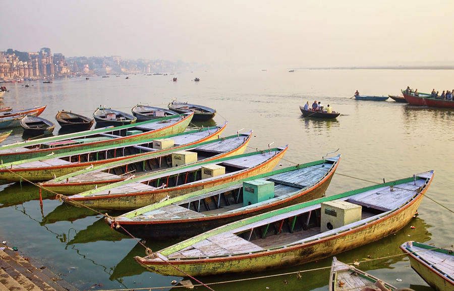 Varanasi, India Bunch of old wooden colorful boats docked in the bay of Ganges river bank during sunset sunrise against foggy weather. The holy place for hindu religion. Photograph by Arpan Bhatia