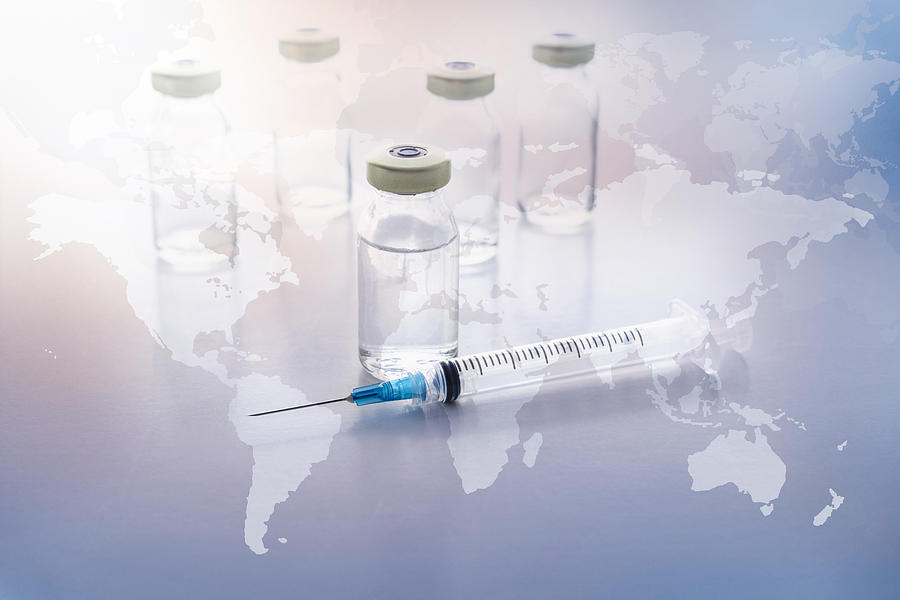 Vials and syringe with world map in background Photograph by Tetra Images
