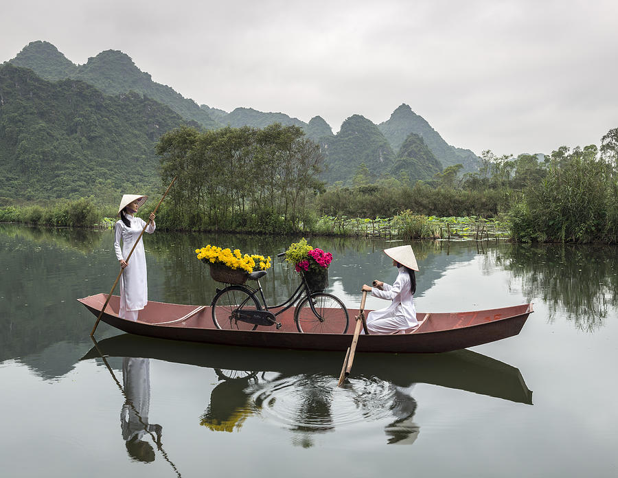 Vietnamese girls rowing boat along river Photograph by Martin Puddy