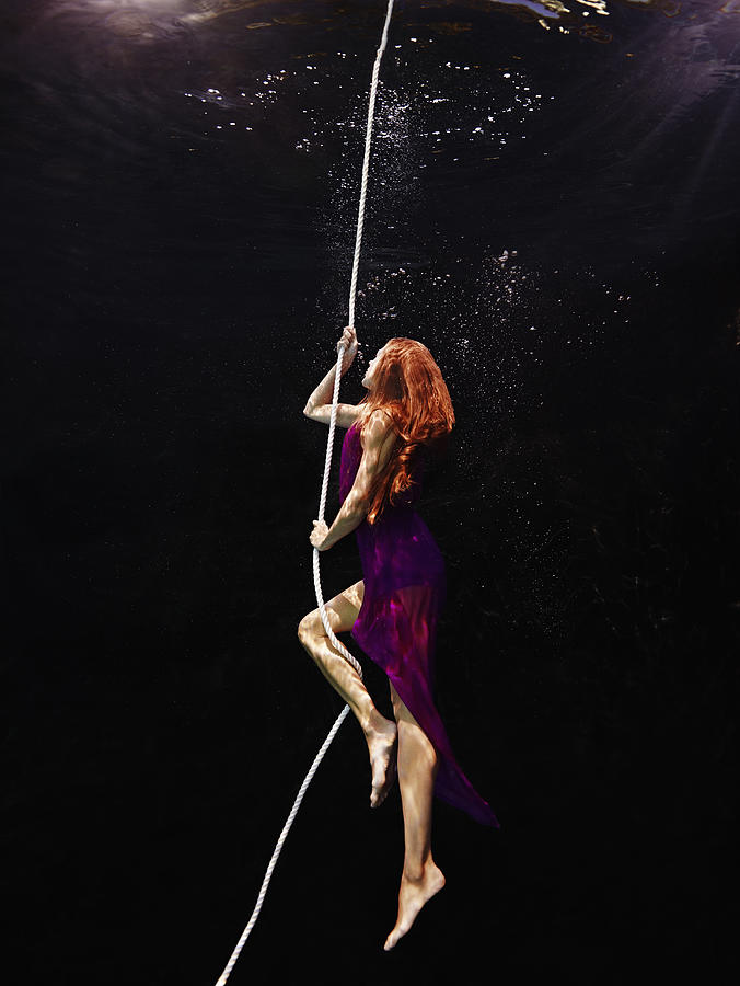 View from underwater of woman climbing up rope Photograph by Thomas Barwick