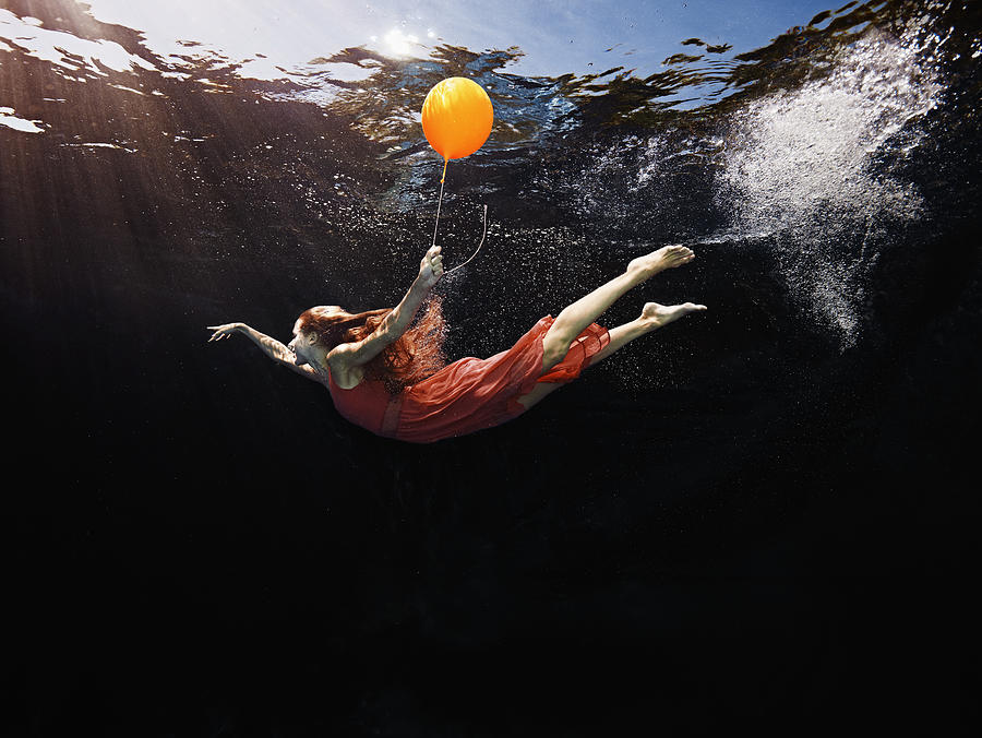 View from underwater of woman holding balloon Photograph by Thomas Barwick