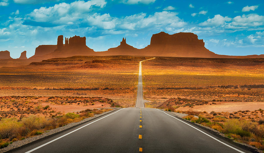 View of historic U.S. Route 163 running through famous Monument Valley in beautiful golden evening light at sunset on a beautiful sunny day with blue sky in summer, Utah, USA Photograph by TravelCouples