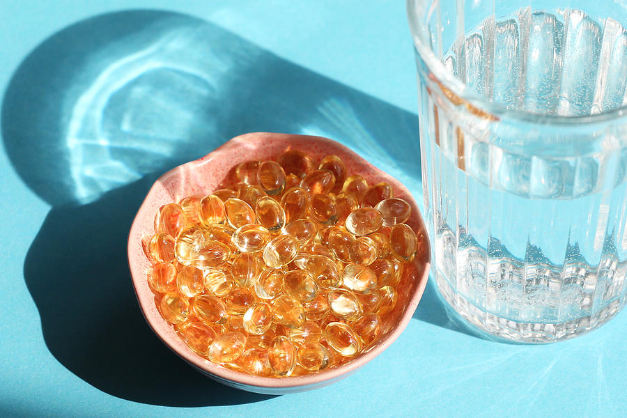 Vitamin D Capsules Next The Glass Of Water On Blue Background Photograph by Elena Popova