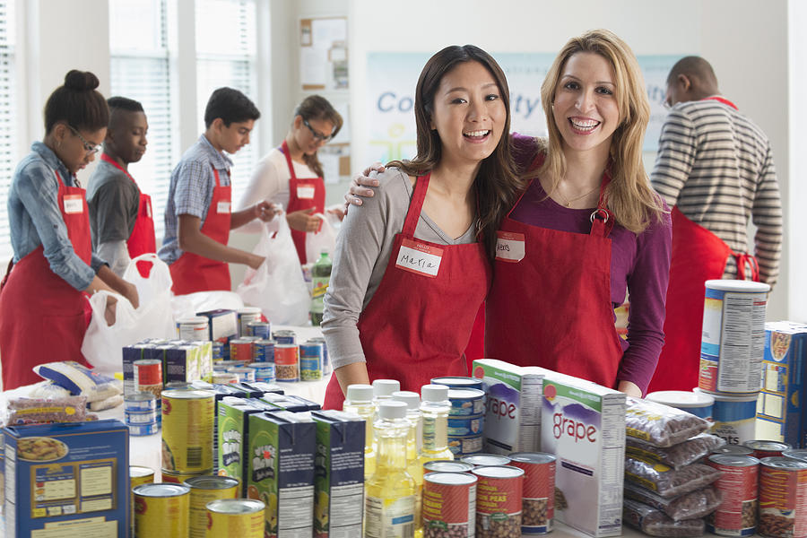 Volunteers smiling near canned goods at food drive Photograph by Jose Luis Pelaez Inc