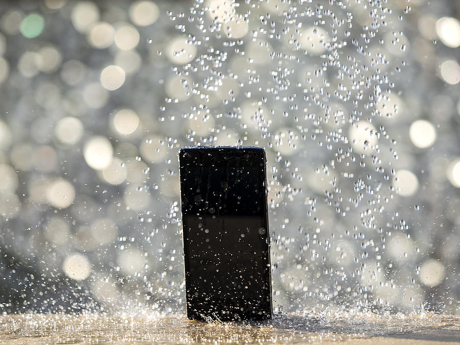 Water jet striking on a wet mobile phone, outdoors illuminated by sunlight Photograph by Jose A. Bernat Bacete