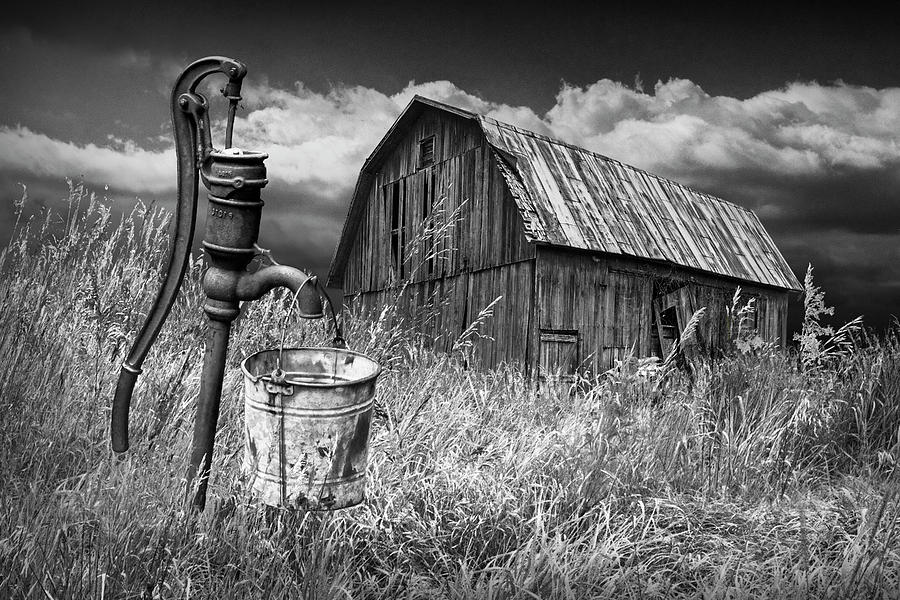 Weathered Wooden Barn With Water Pump And Metal Bucket In Black And White Photograph