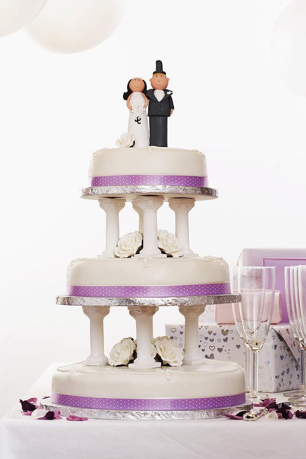 Wedding cake decorated with bride and groom figures on table by gifts Photograph by Martin Poole