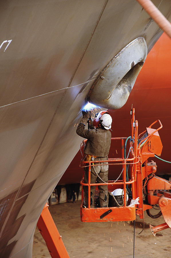 Welder working on side of ship in dry dock, standing on cherry-picker Photograph by Kevin Phillips