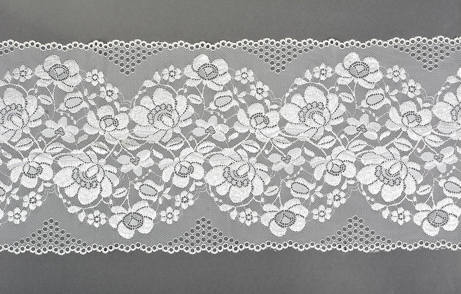 white color straight strip of lace fabric on gray background. Elastic silk nylon braid border. use clothes linen decoration. repeating pattern and interweaving threads. Photograph