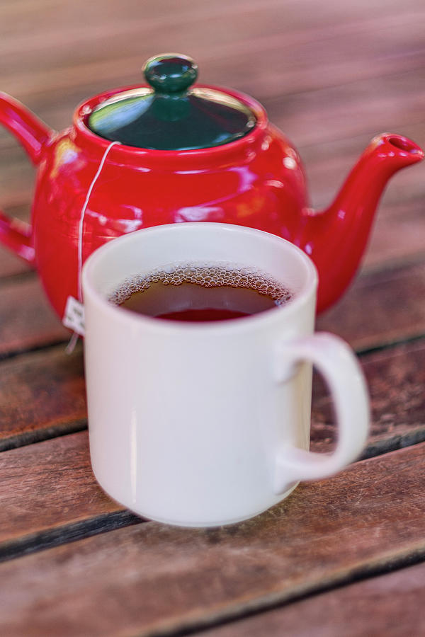 White mug filled with black tea next to red porcelain teapot on  Photograph by David L Moore