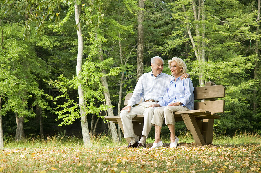 White senior couple sitting on a park bench in the forest  Photograph by FlashSG