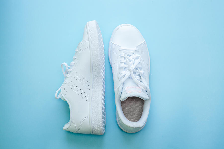 White sports shoes over blue background, sports and casual clothing style concept. Summer or spring fashion. Photograph by Anna Blazhuk