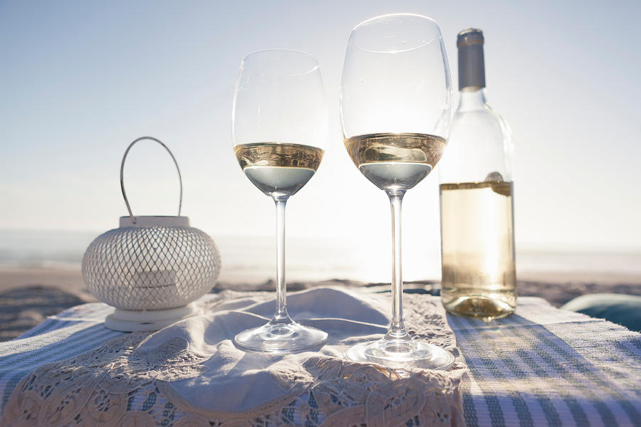 White wine, glasses and candle on beach Photograph by Cultura RM Exclusive/GretaMarie