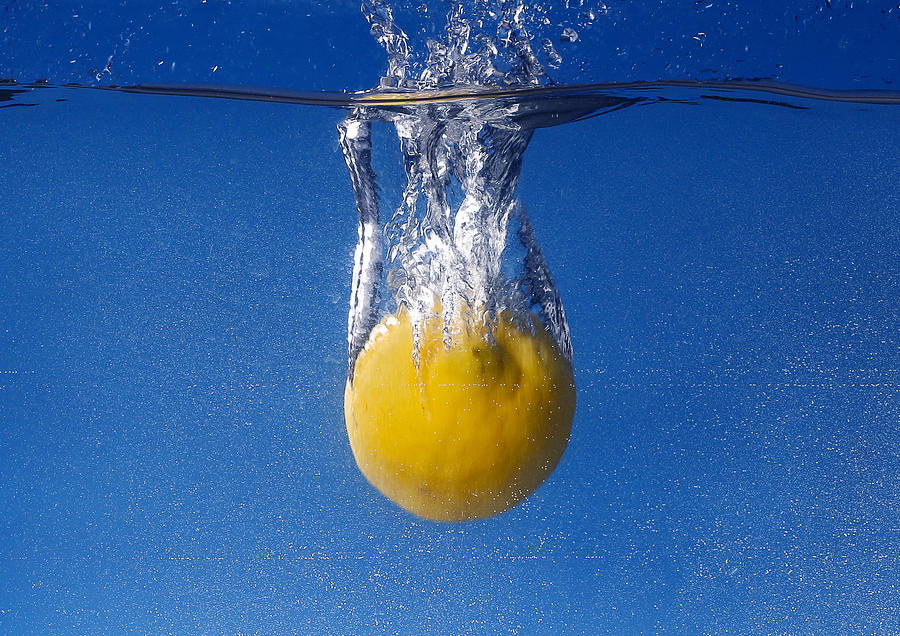 Whole lemon dropped in water against gradient blue background Photograph by Santiaga