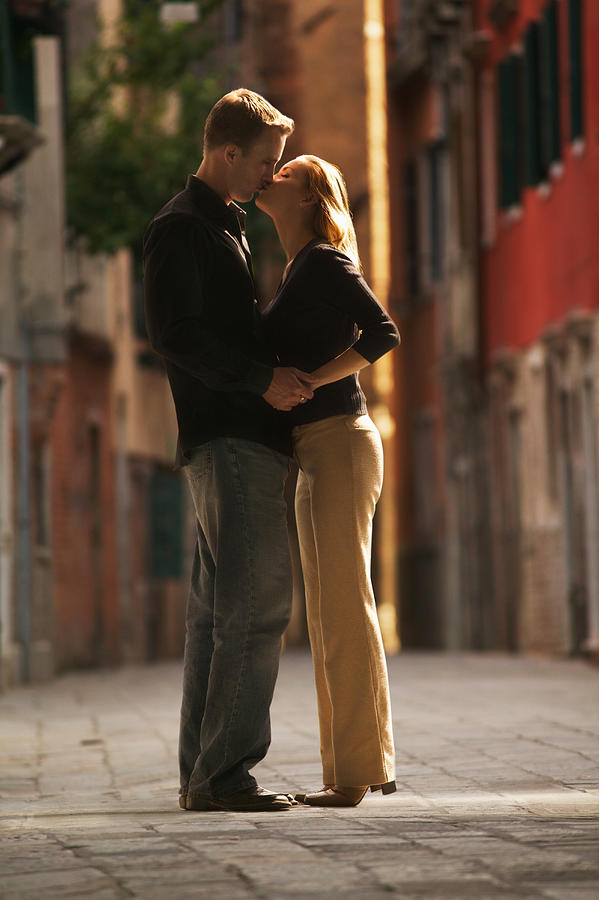 Wide Shot Of A Young Adult Couple As They Hug And Kiss On An Old Cobblestone Road Photograph by Photodisc