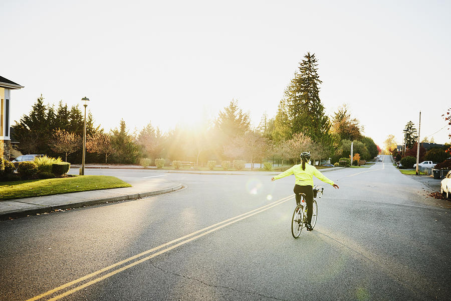 Wide shot of mature woman riding road bike with arms outstretched on fall evening Photograph by Thomas Barwick