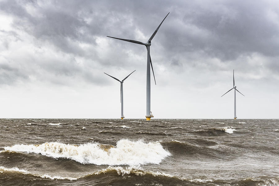 Wind turbines in an offshore wind park during a storm with big waves hitting the shore Photograph by Sjo