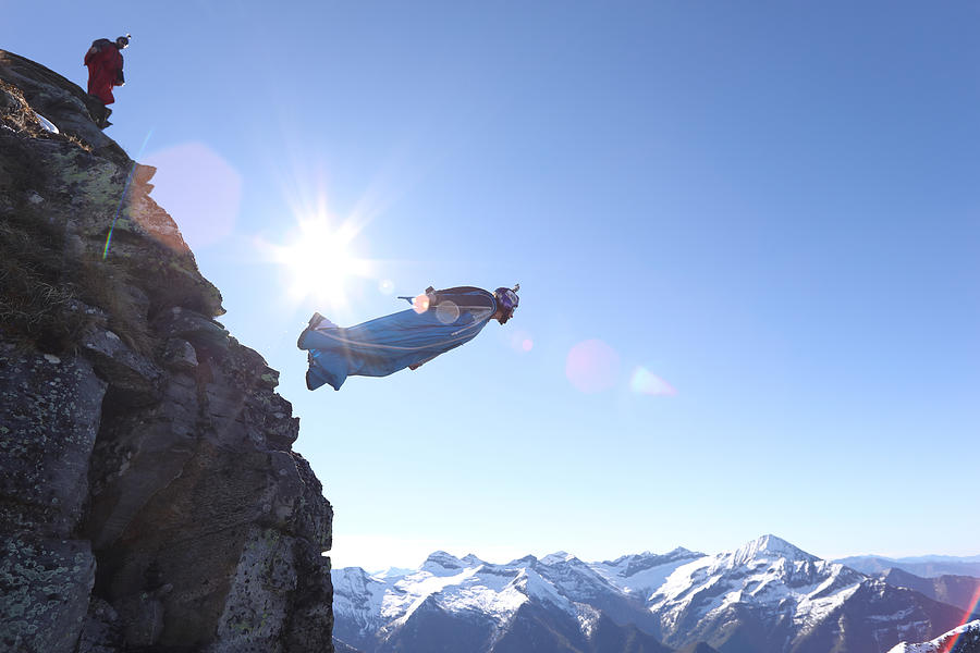 Wingsuit flyer jumps from cliff edge, mountains Photograph by Ascent/PKS Media Inc.