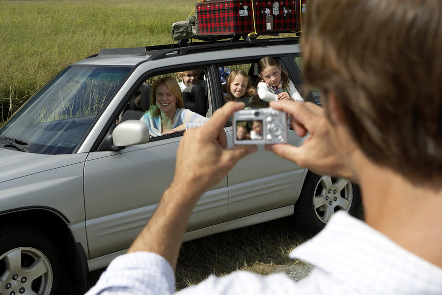 Woman and children (6-8 years) in car being photographed by man, rear view, in foreground Photograph by Noel Hendrickson