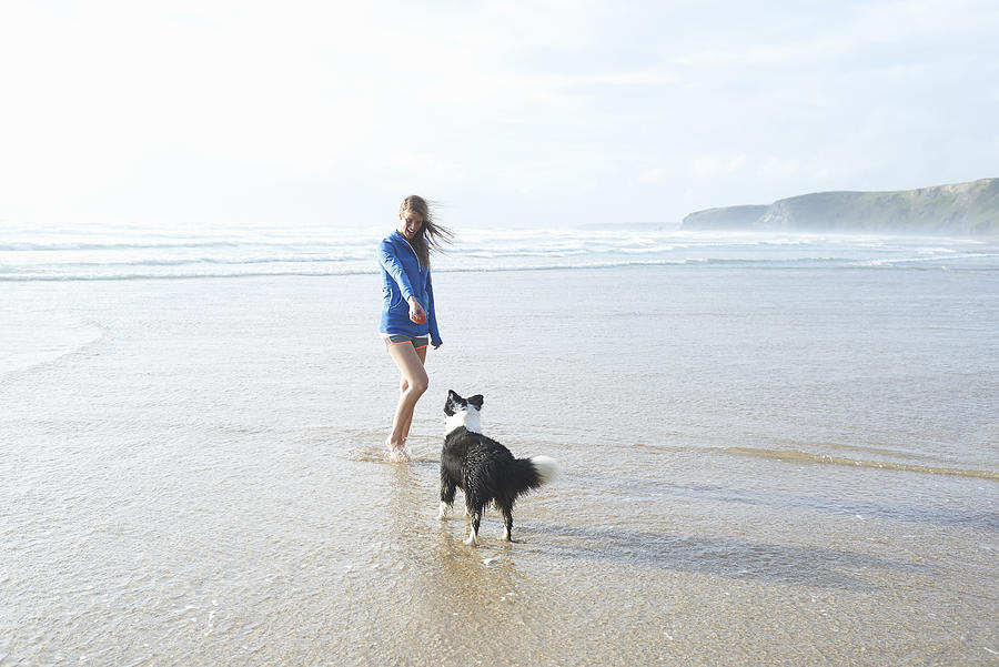 Woman and dog playing at beach. Photograph by Dougal Waters