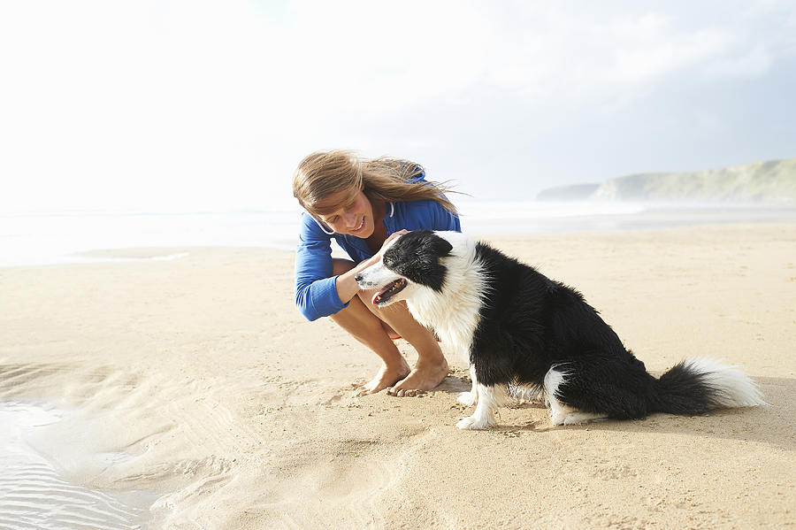 Woman and dog sitting on beach. Photograph by Dougal Waters