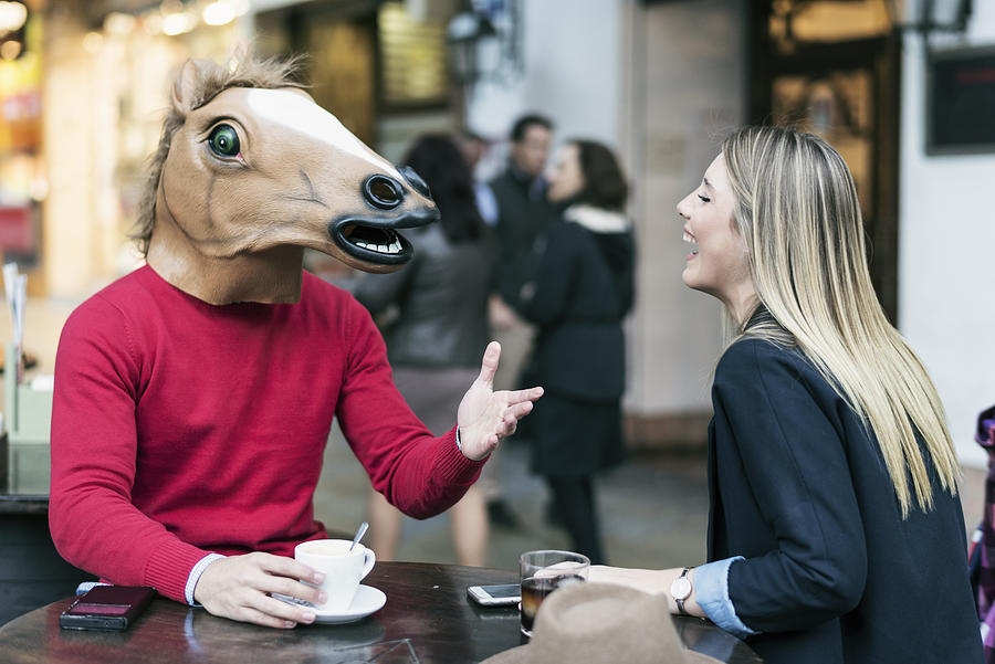 Woman and horse face man with costume drinking coffee in bar terrace and talking having fun Photograph by Antonio Garcia Recena