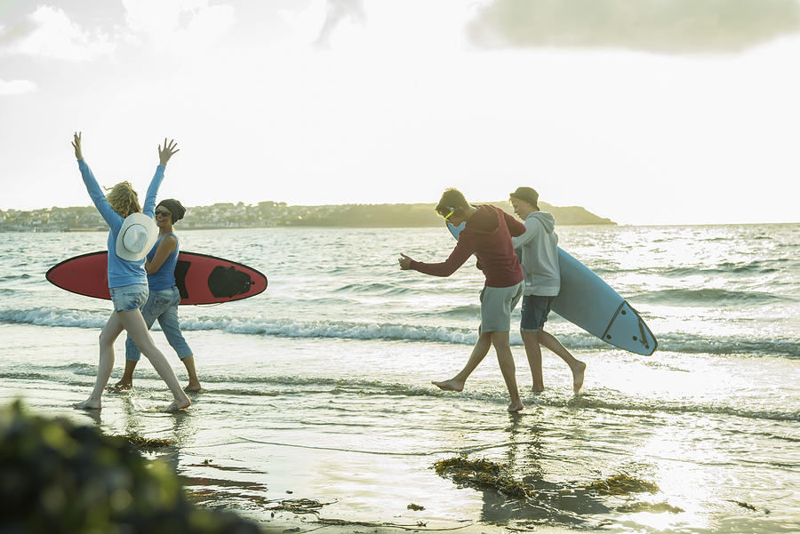Woman and three teenagers with surfboards running at waterside of the sea Photograph by Westend61