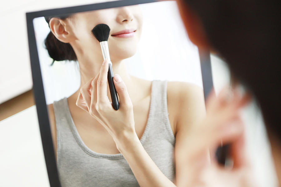 Woman applying blush in mirror Photograph by Runstudio