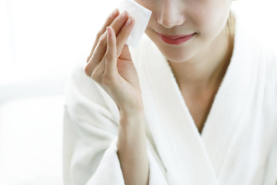 Woman applying cleansing lotion to face, using cotton wool pad Photograph by Runstudio