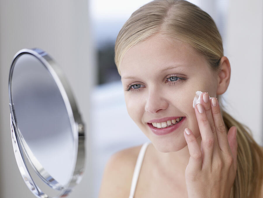 Woman applying lotion or cream to face in mirror Photograph by Chris Ryan