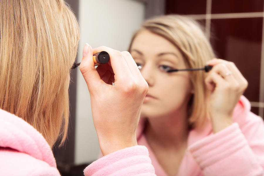 Woman applying mascara on eyelashes Photograph by Fotek