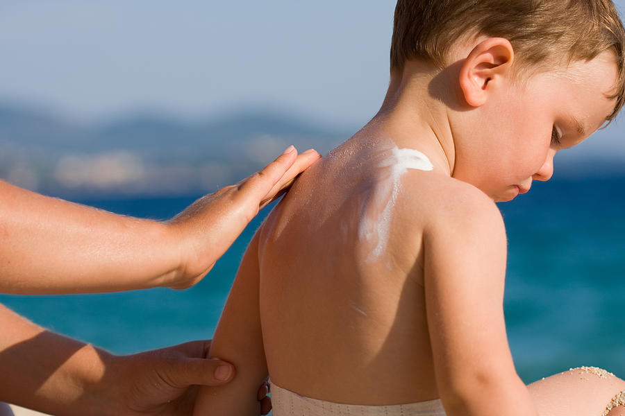 Woman applying sunscreen on a childs back at the beach Photograph by firemanYU